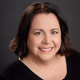 Smiling middle-aged woman with shoulder-length dark hair wearing a black top and grey background.