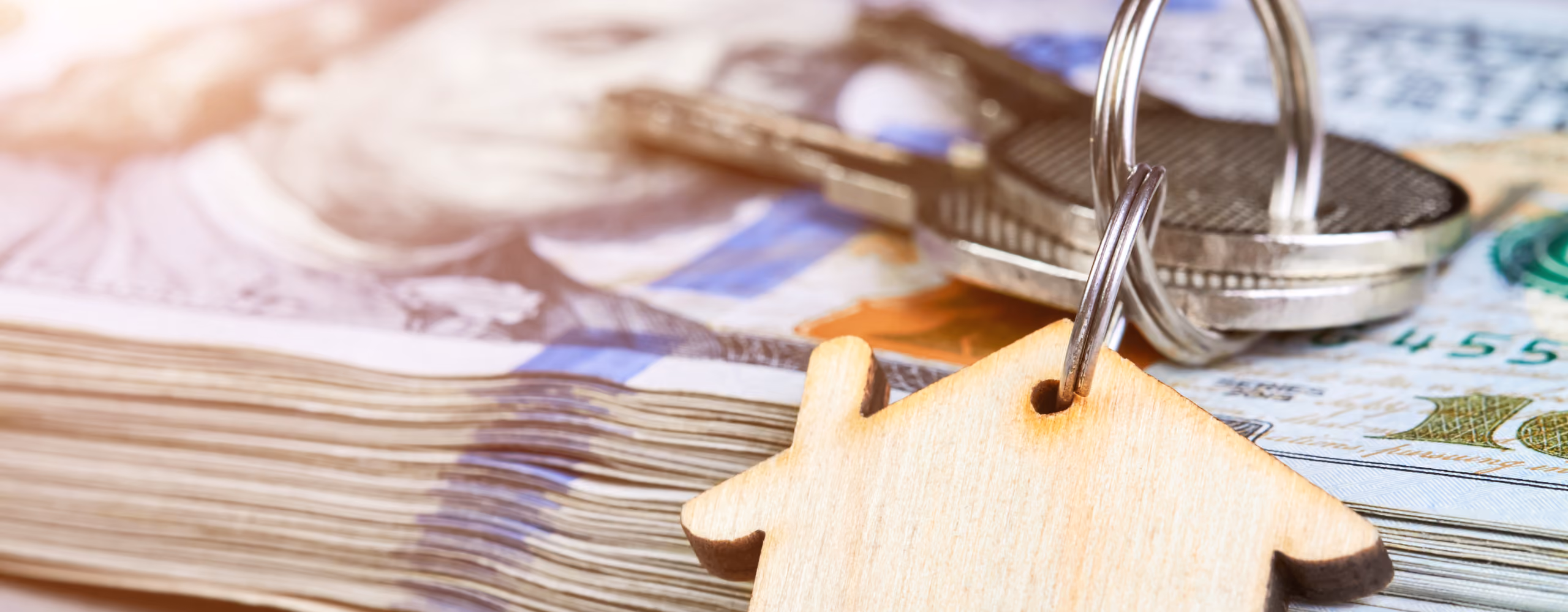 House-shaped keychain and keys on top of a stack of US hundred-dollar bills.