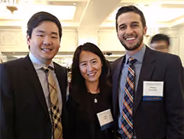 Three people smiling, dressed in business attire, with name tags at a formal indoor event.