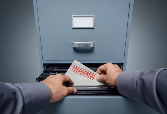 Person placing a document labeled confidential into an open filing cabinet drawer.