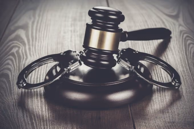 Judge’s gavel resting on wooden block with metal handcuffs on a wooden surface.