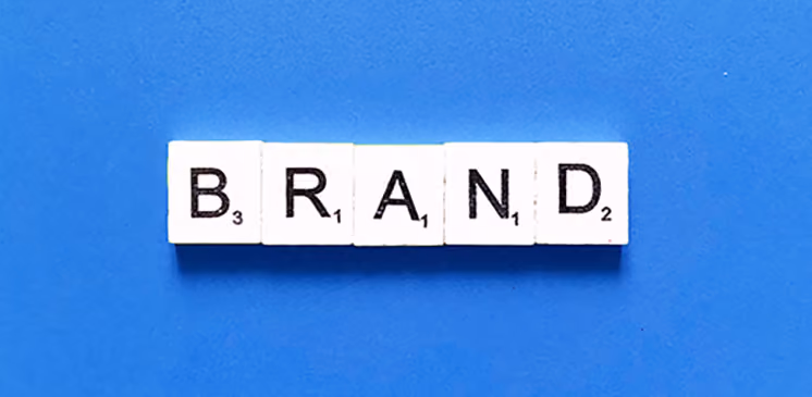 Scrabble tiles spelling the word BRAND on a blue background.