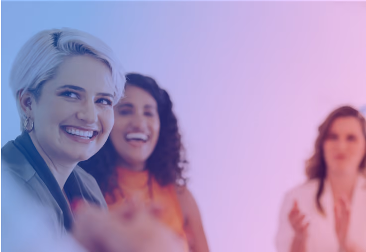 Three women smiling and engaging in a lively conversation with a purple and blue gradient background.