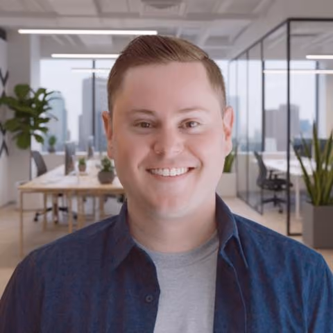 Smiling man with short hair wearing a blue shirt and gray t-shirt in a modern office setting.