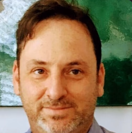 Close-up of a man with short dark hair and beard smiling in front of a green and white abstract background.