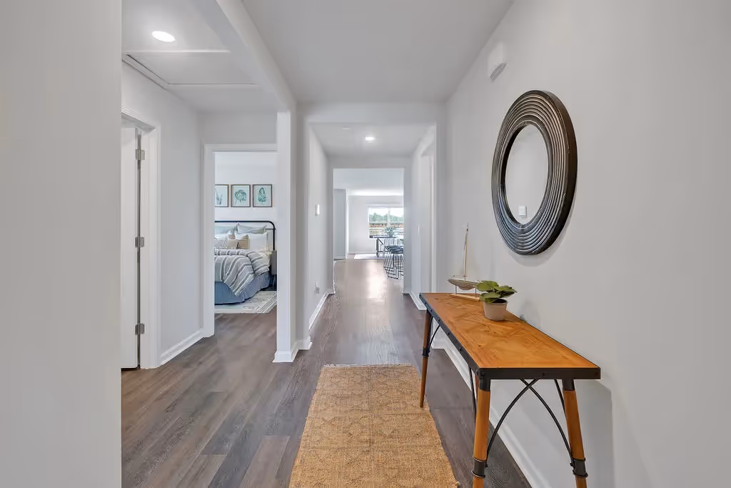 Inviting entryway and hallway of a Landing at Stone Chimney home, Supply NC, with dark wood flooring, a decorative console table, and glimpses of a bedroom and living area