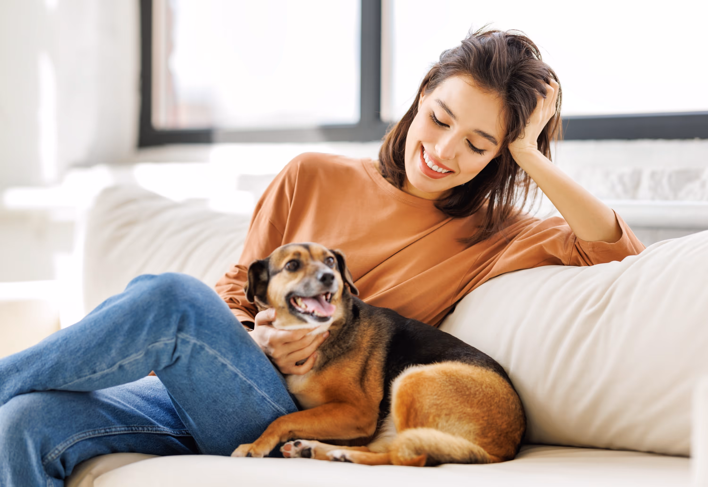 A smiling woman relaxing on a sofa and petting her small dog, representing the comfortable and pet-friendly home life at The Landing at Stone Chimney in Supply, NC.