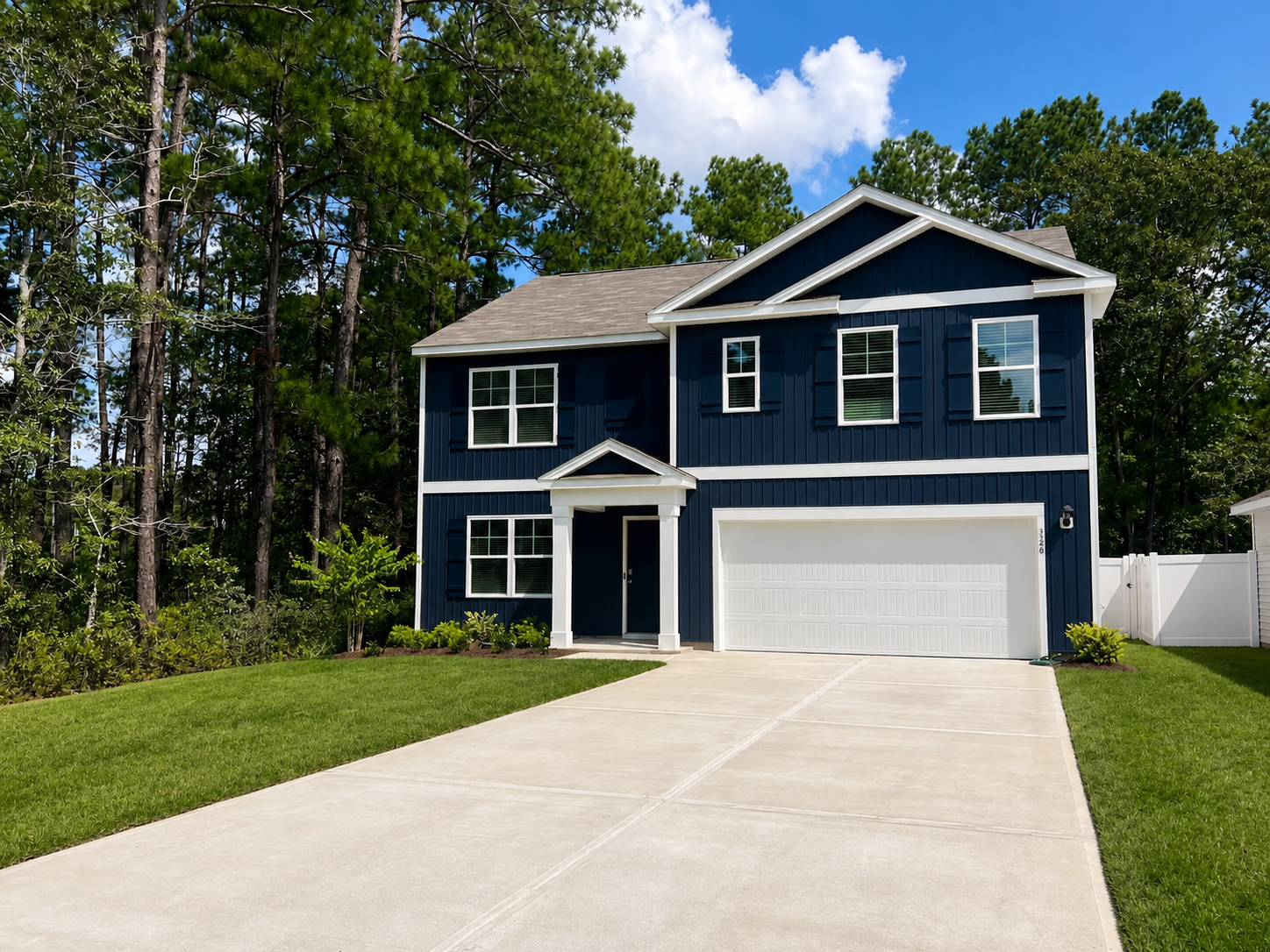 Large two-story navy blue house at Landing at Stone Chimney, Supply NC, with white trim and a white garage door, surrounded by tall pine trees