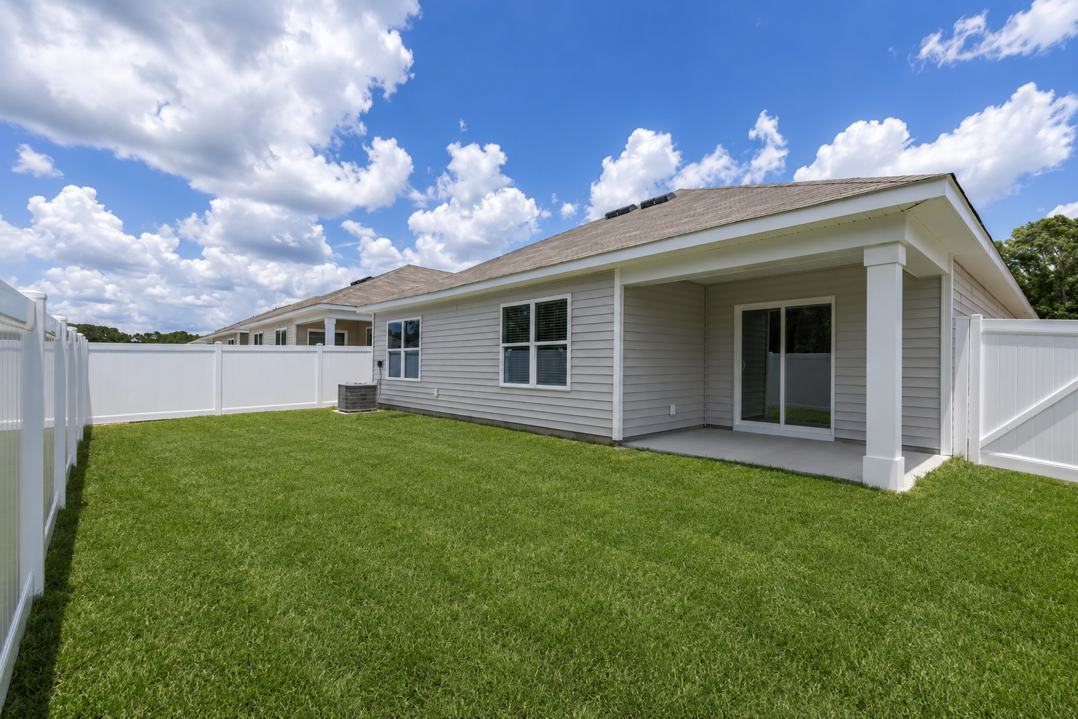 Spacious backyard of a new home at Landing at Stone Chimney, Supply NC, with green grass, white vinyl fence, and covered patio