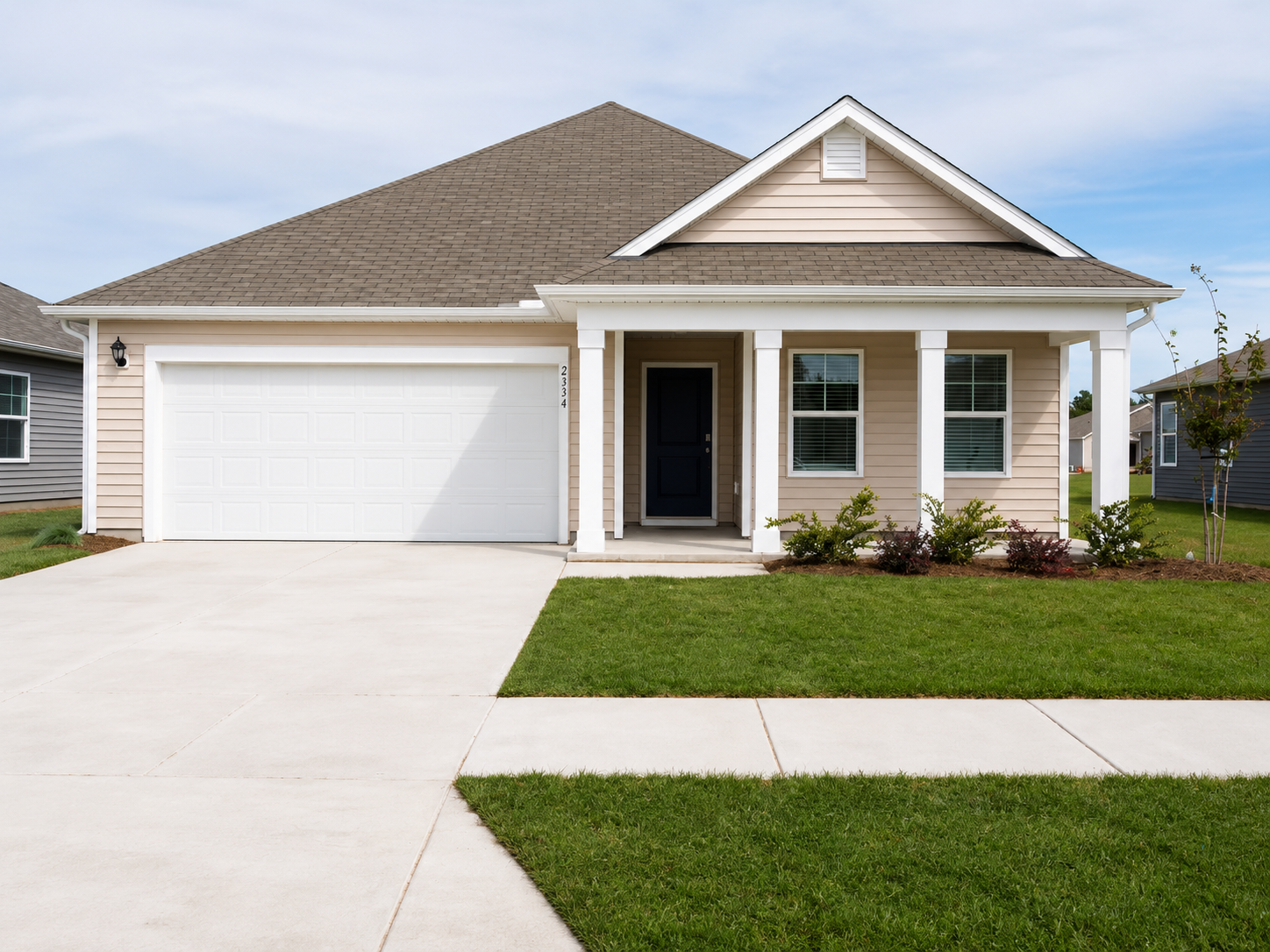 Newly built single-story beige house at Landing at Stone Chimney, Supply NC, with white pillars, dark blue front door, and white garage door