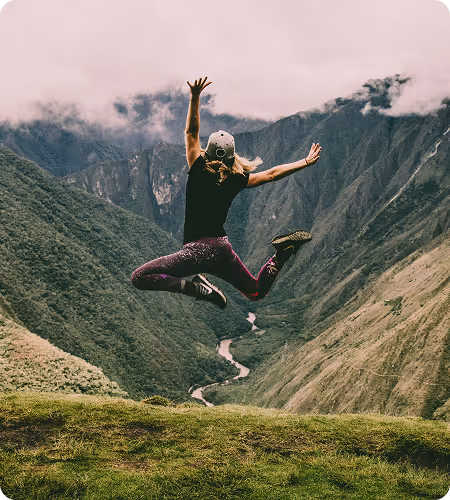 A healthy woman jumping of joy looking at a beautiful mountain landscape