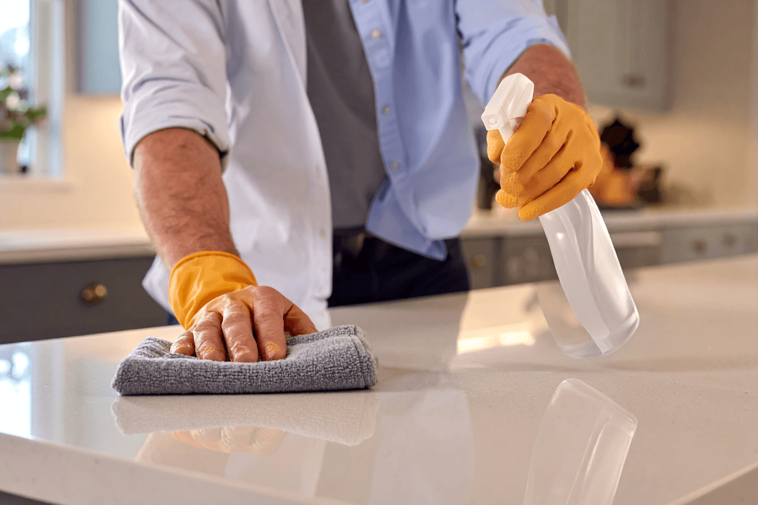 Person wearing yellow gloves cleaning a countertop with a spray bottle and cloth.