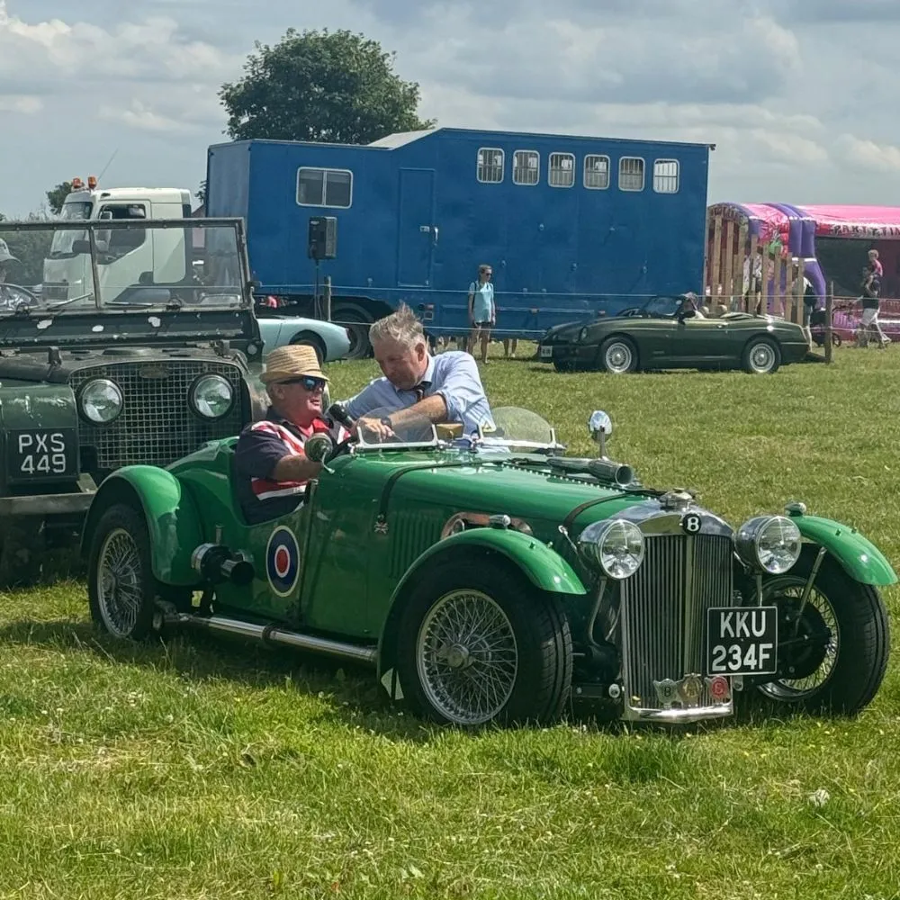A man in an old, green car with a war time roundel on the door getting interviewed.