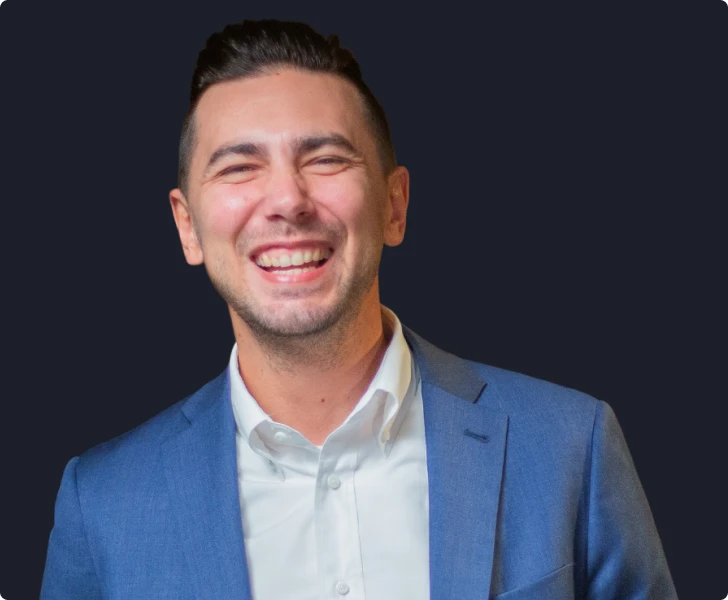 Professional headshot of person smiling against blurred office background, wearing blazer