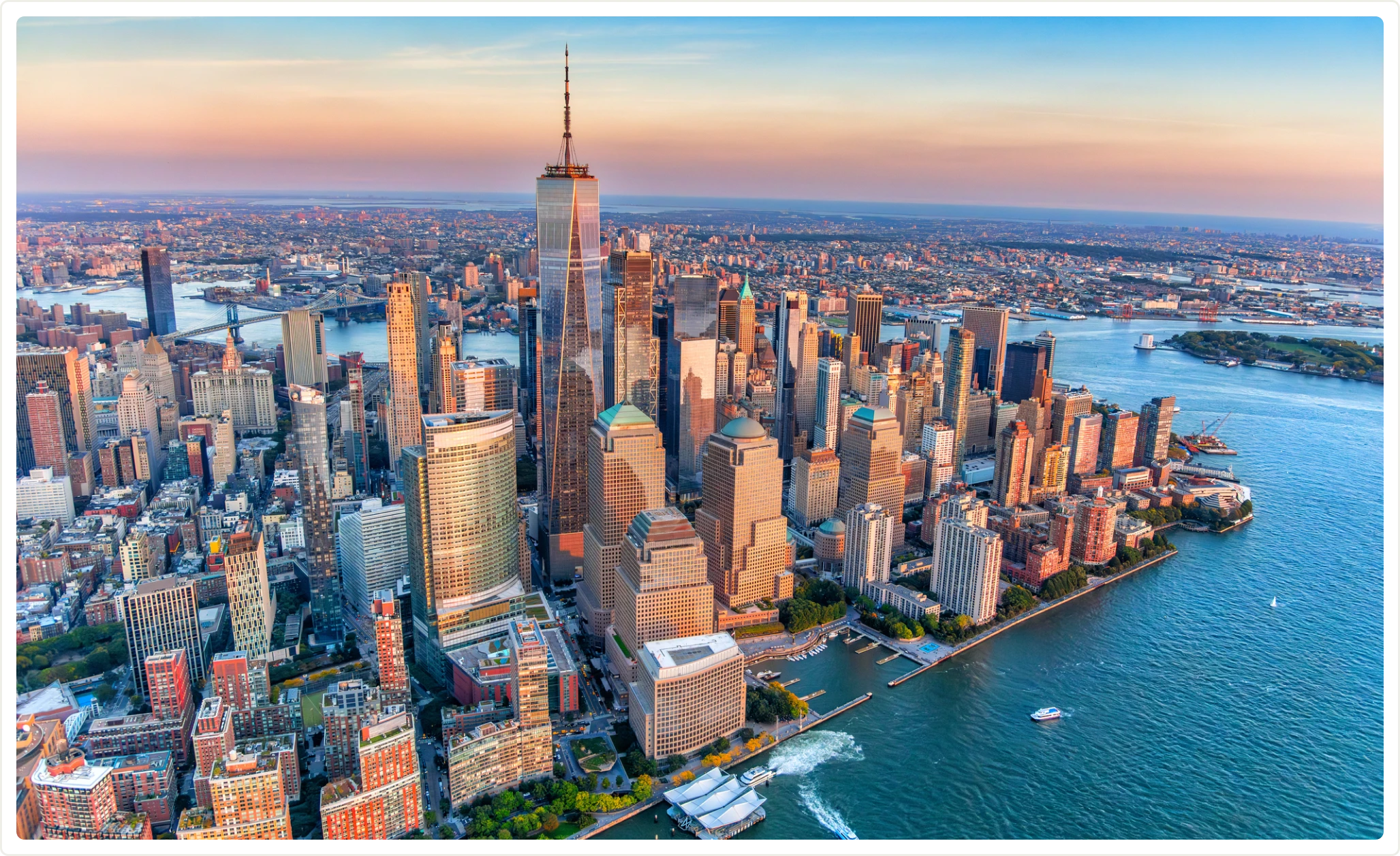Aerial view of New York City skyline at sunset with skyscrapers and water surrounding the lower Manhattan area.