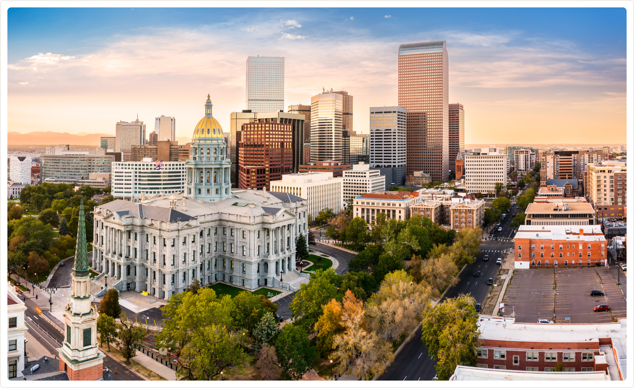 Denver skyline at sunset with the Colorado State Capitol and downtown skyscrapers surrounded by trees.