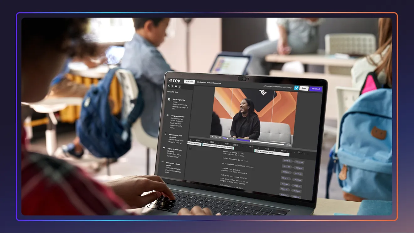 Person typing on laptop showing video captioning software in classroom with students and backpacks.