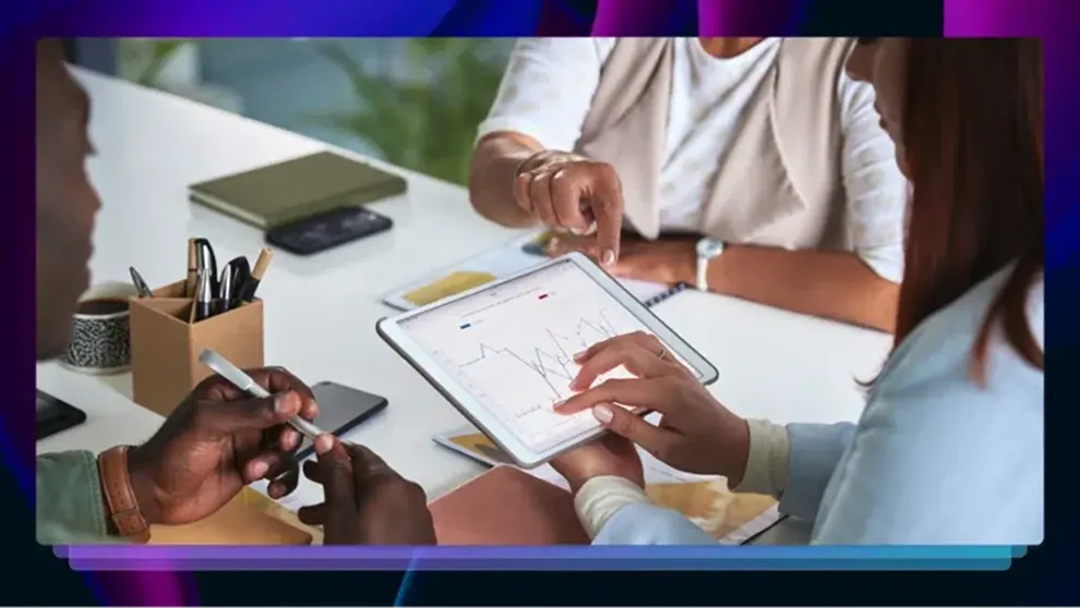 Two colleagues discuss data shown on a tablet with graphs and charts at a white table.