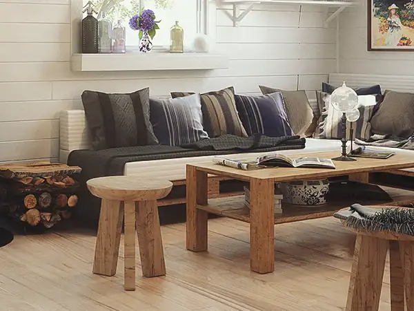 Gemütliches Wohnzimmer mit schwarzem Holzofen, Holzbalken, Sofa mit Kissen und rustikalem Holztisch mit Hockern