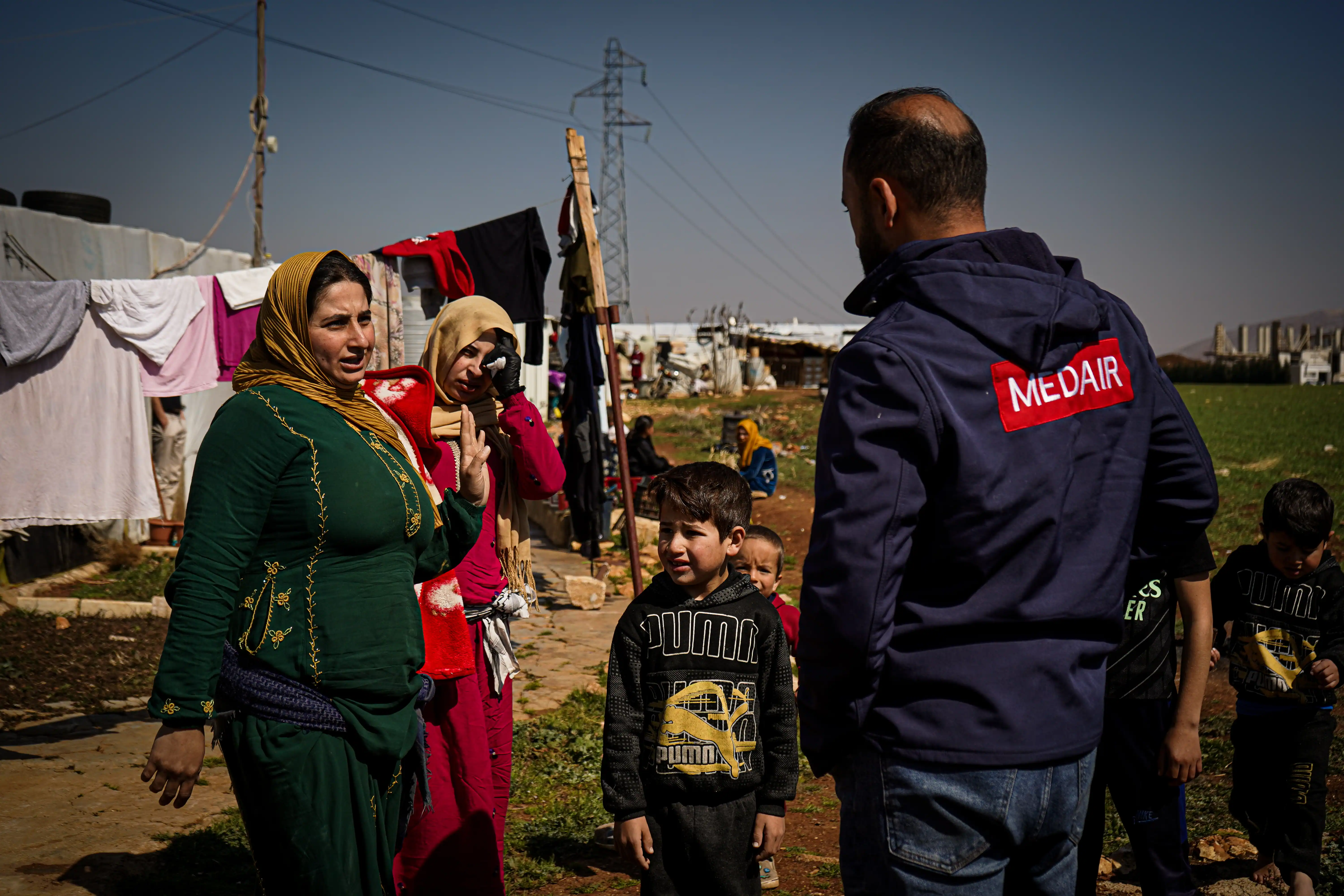 Syrian refugees speak with a humanitarian aid worker at an informal settlement.