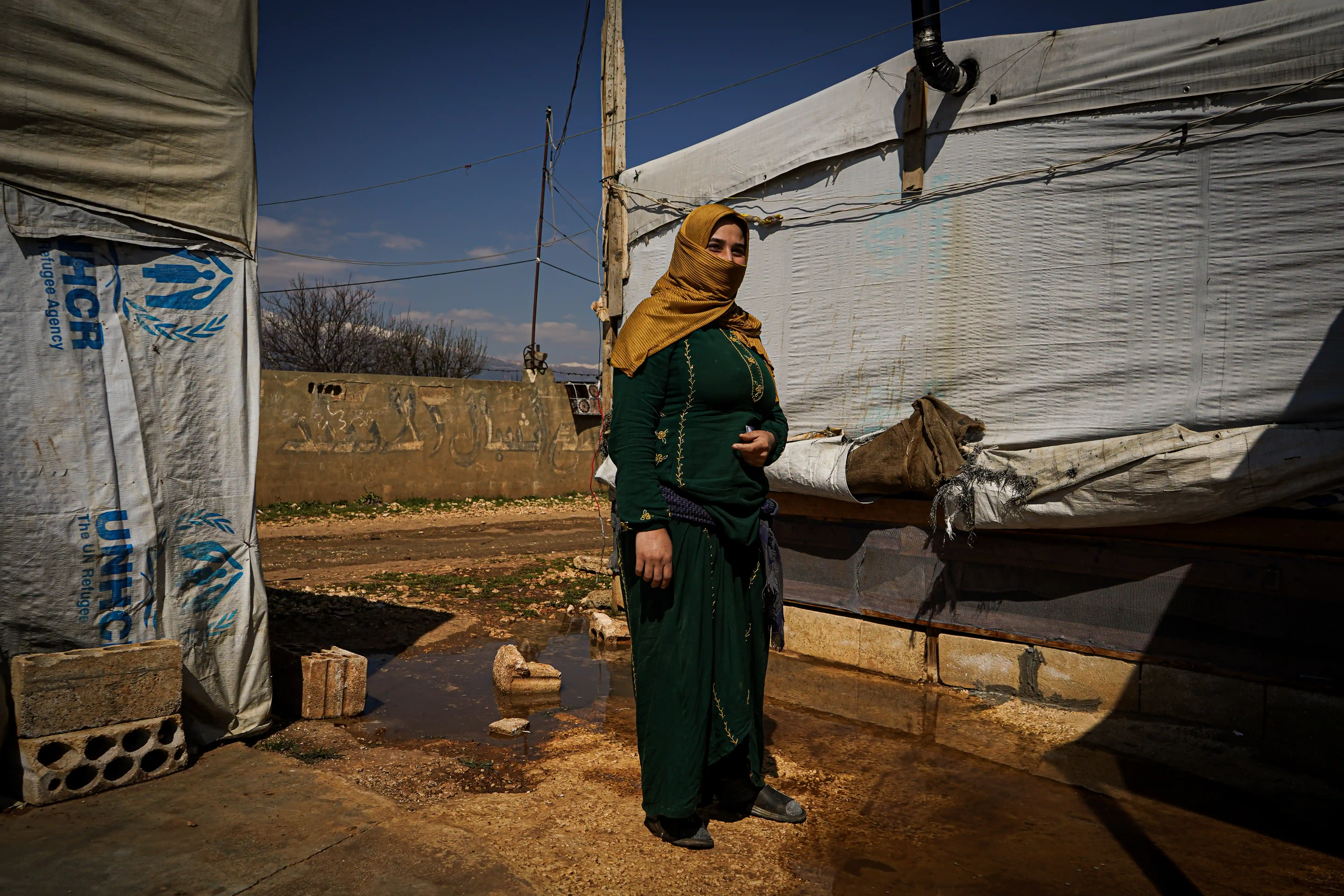 A Syrian refugee stands next to her tented home affected by harsh weather conditions in an informal settlement.