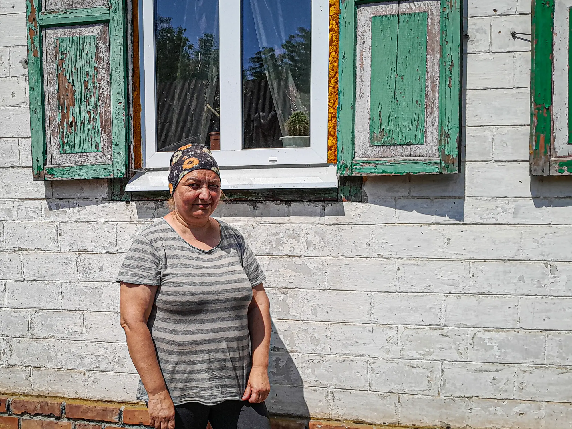 Woman standing by her brick house with new windows and visible construction materials on the ground. 