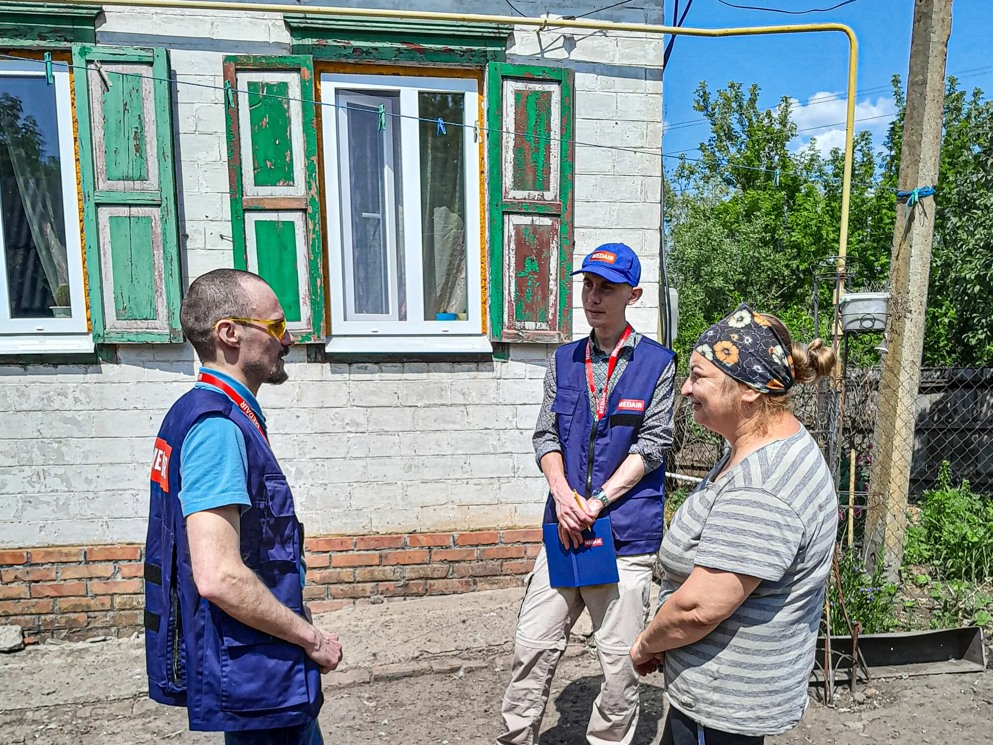 Medair staff talking to a local woman outside a repaired home with new windows in rural Ukraine. 