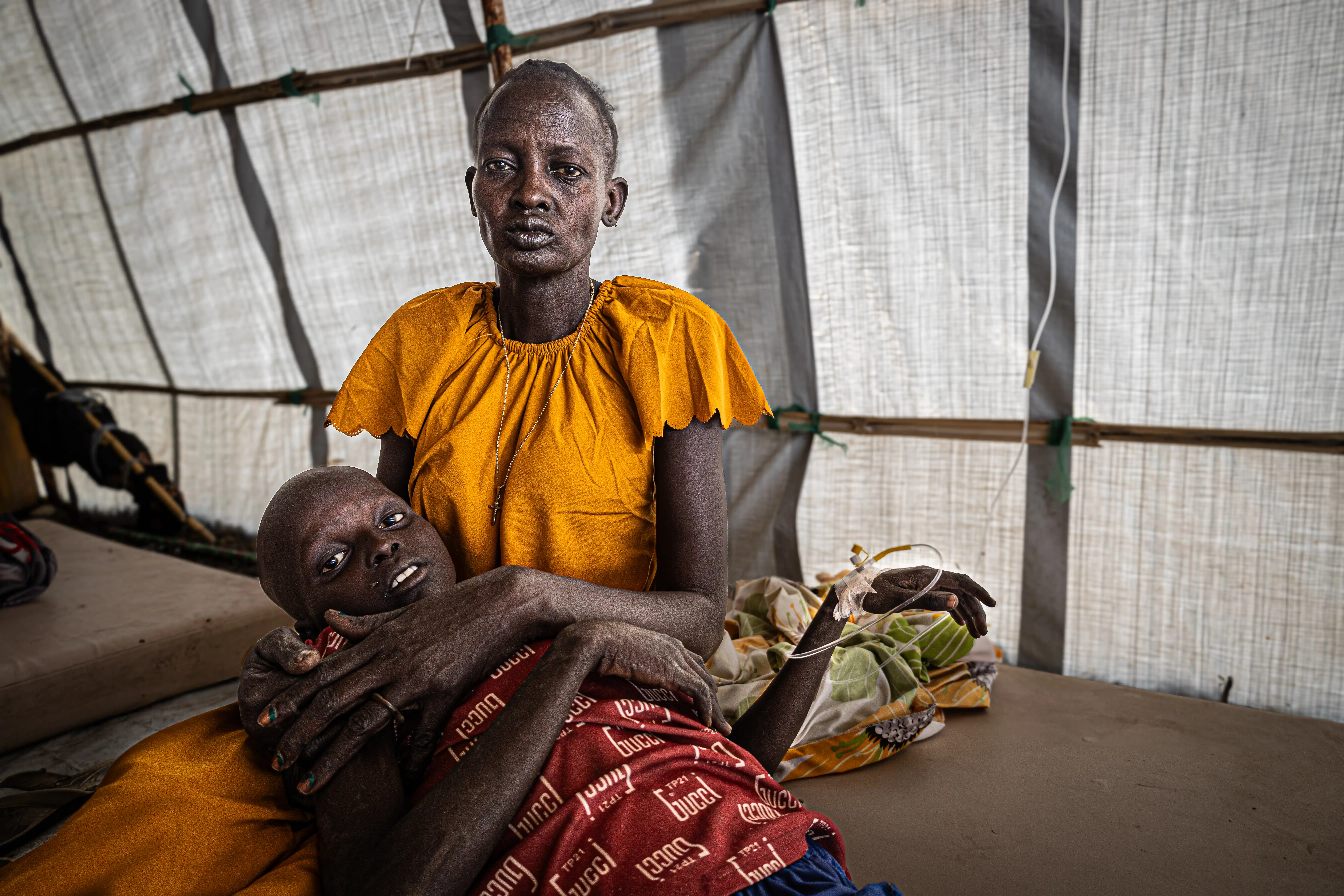 A woman holds her son, who is lying on a cot with an IV attached, inside a cholera treatment unit.