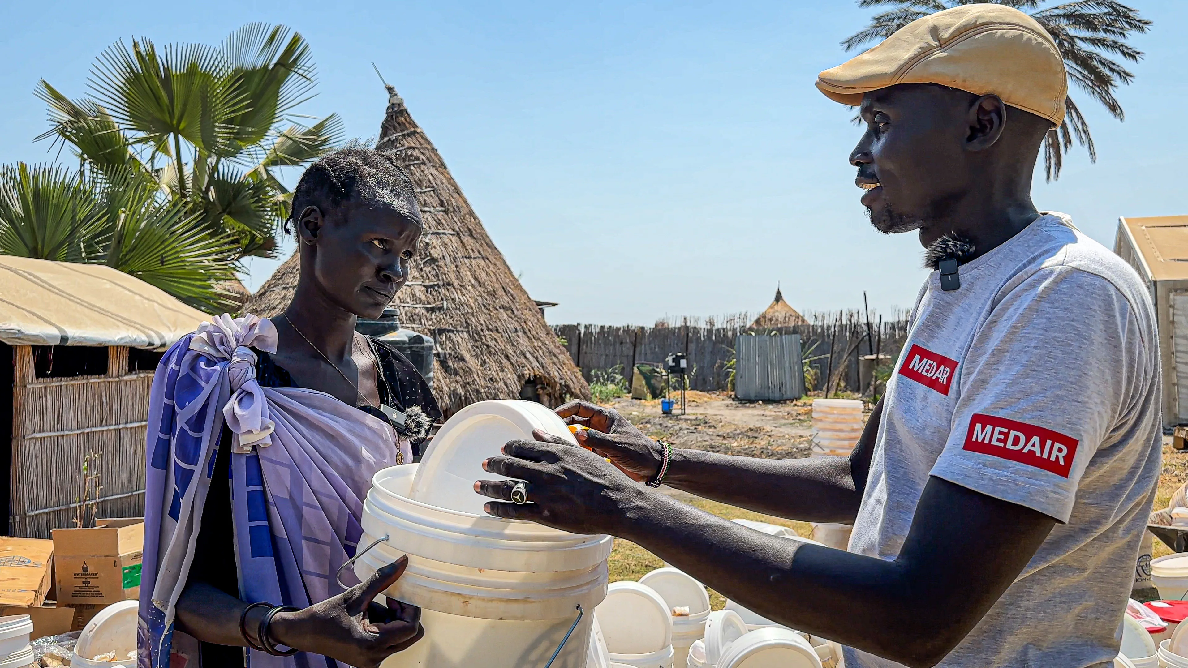A Medair worker hands over a covered bucket to a woman during a hygiene kit distribution outside in a village.