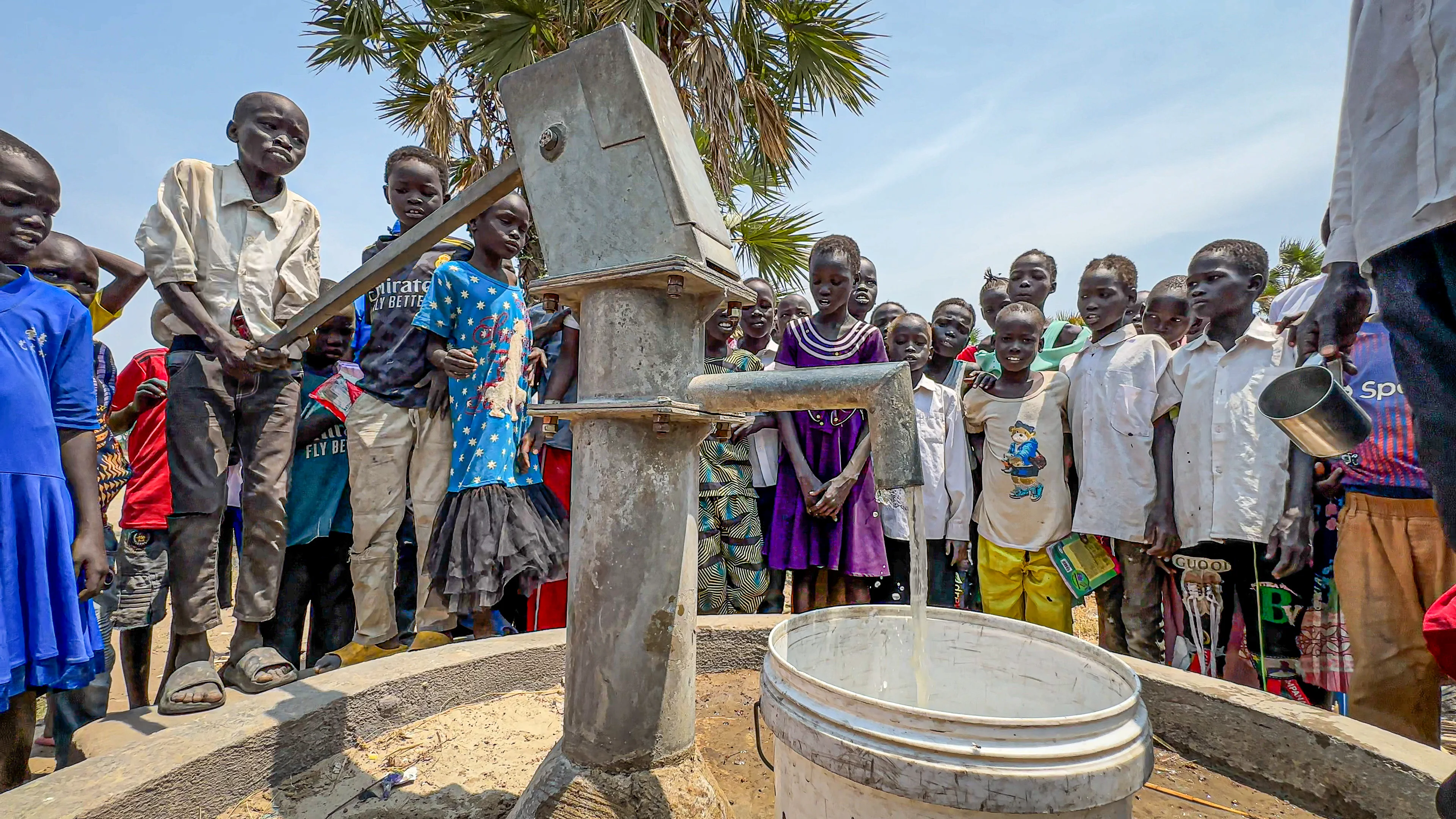 A school boy pumps water with a handpump in South Sudan while other pupils are watching.
