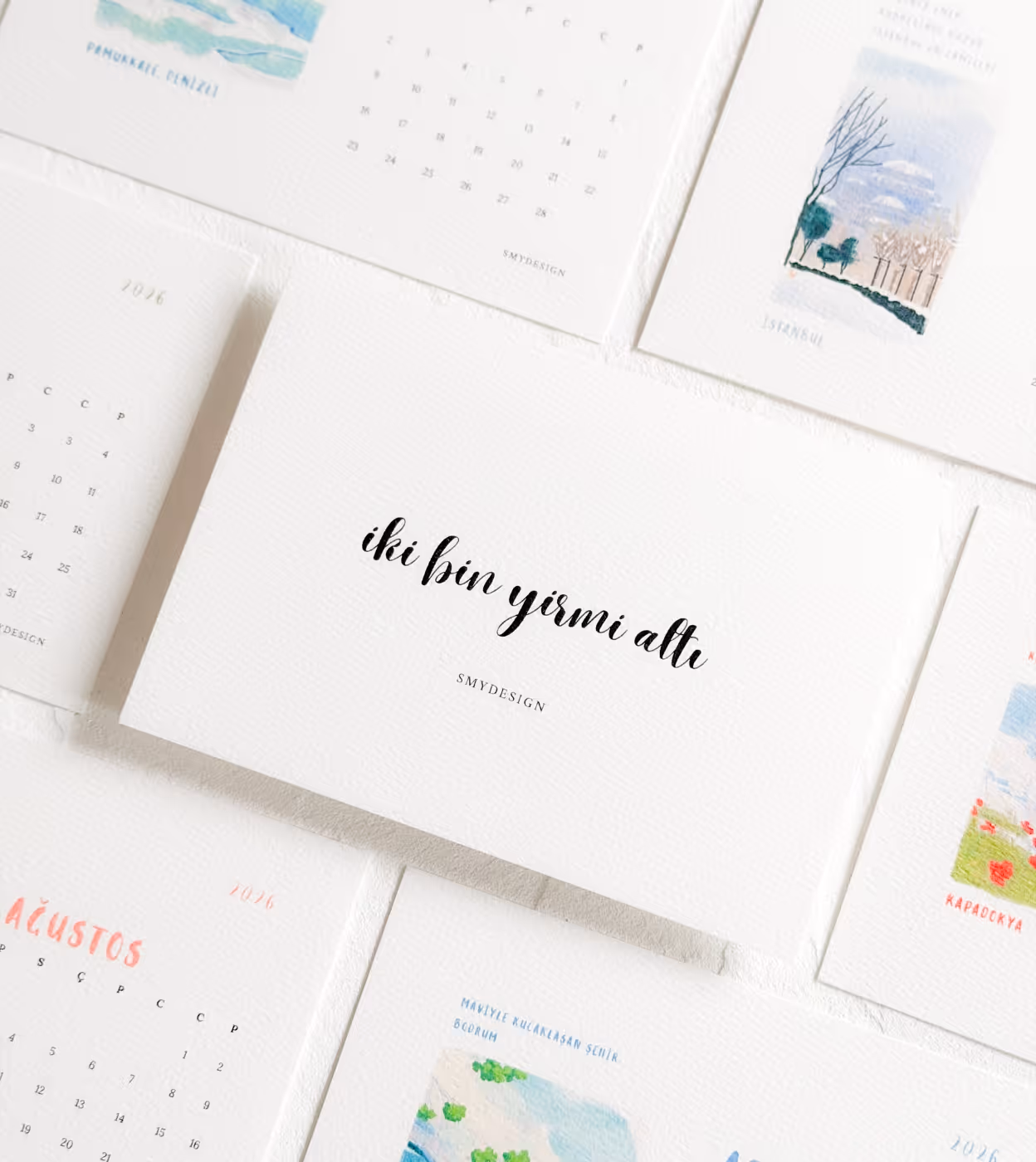 Verschiedene Kalenderblätter von Smydesign aus dem Jahr 2026, mit kalligraphischem Text und kleinen Landschaftsillustrationen.