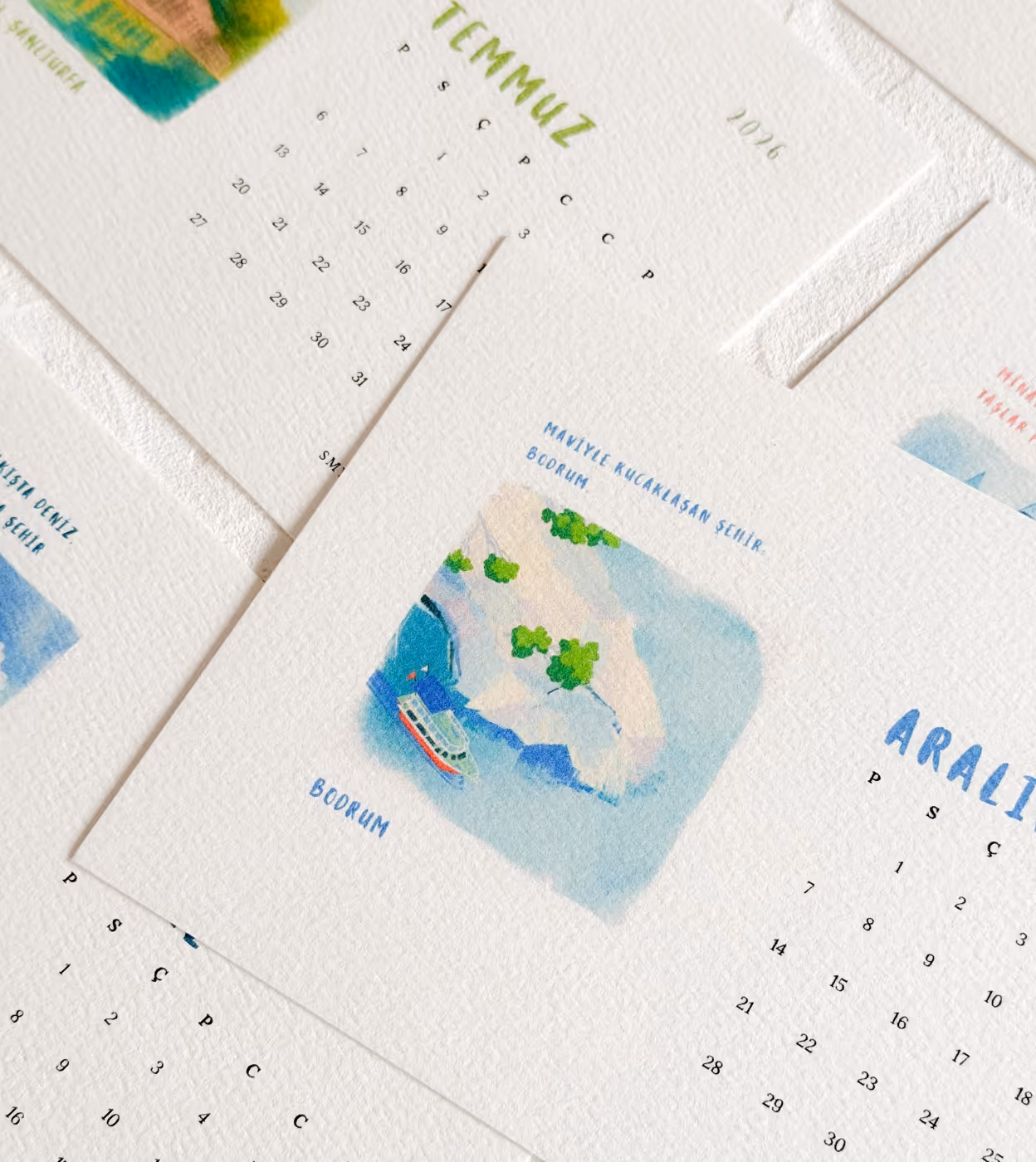 Kalenderblätter mit Aquarellmalereien von Küstenlandschaften und Monatsnamen auf Türkisch.