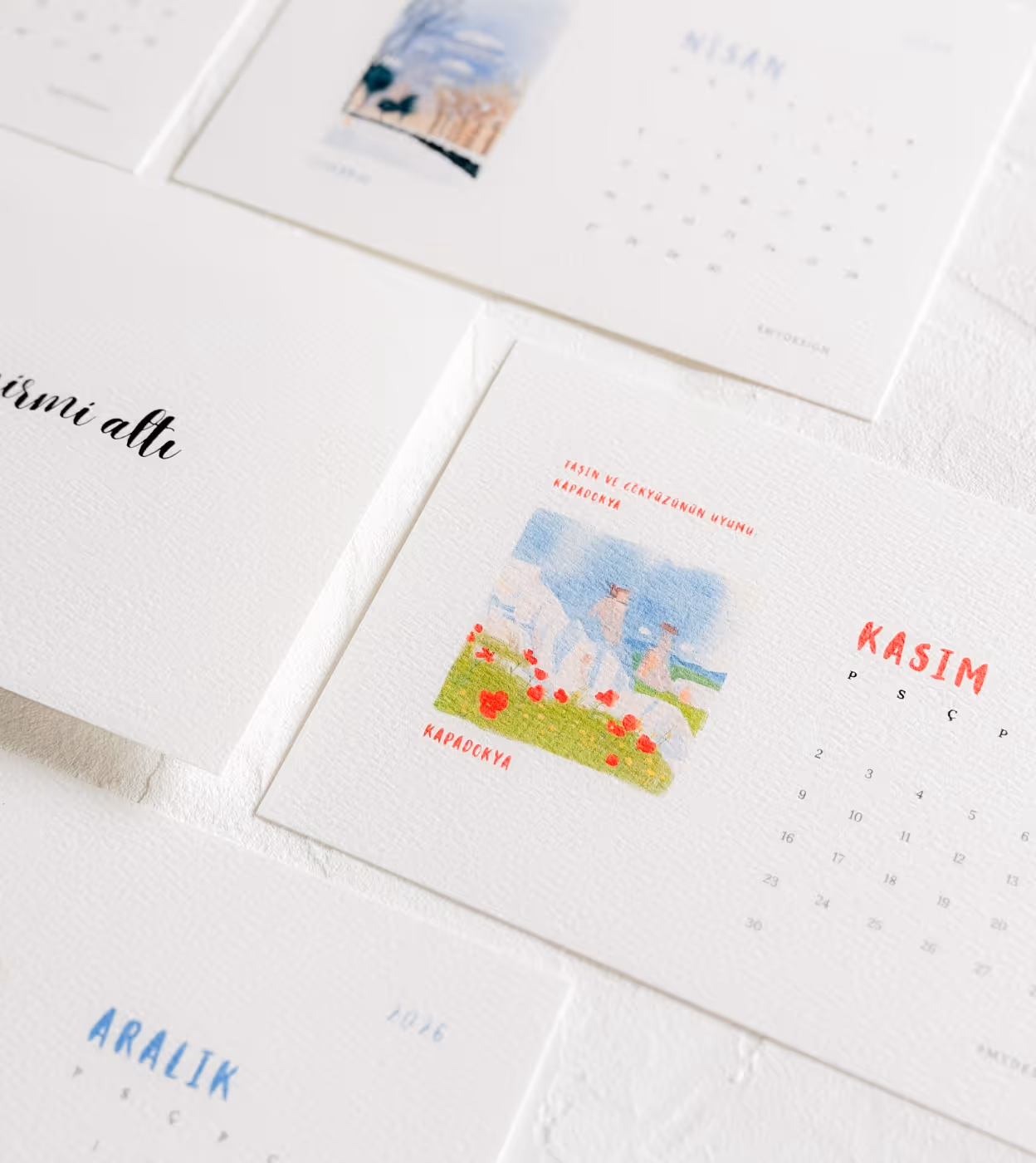 Mehrere Monatskalenderblätter mit minimalistischen Landschaftsbildern und türkischen Monatsnamen auf weißem Hintergrund.