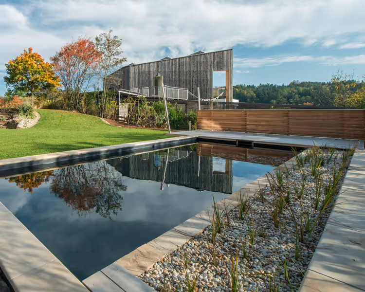 Naturpool mit Kiesfilter und Holzterrasse von Daniel Hofer Gärten gebaut in Graz