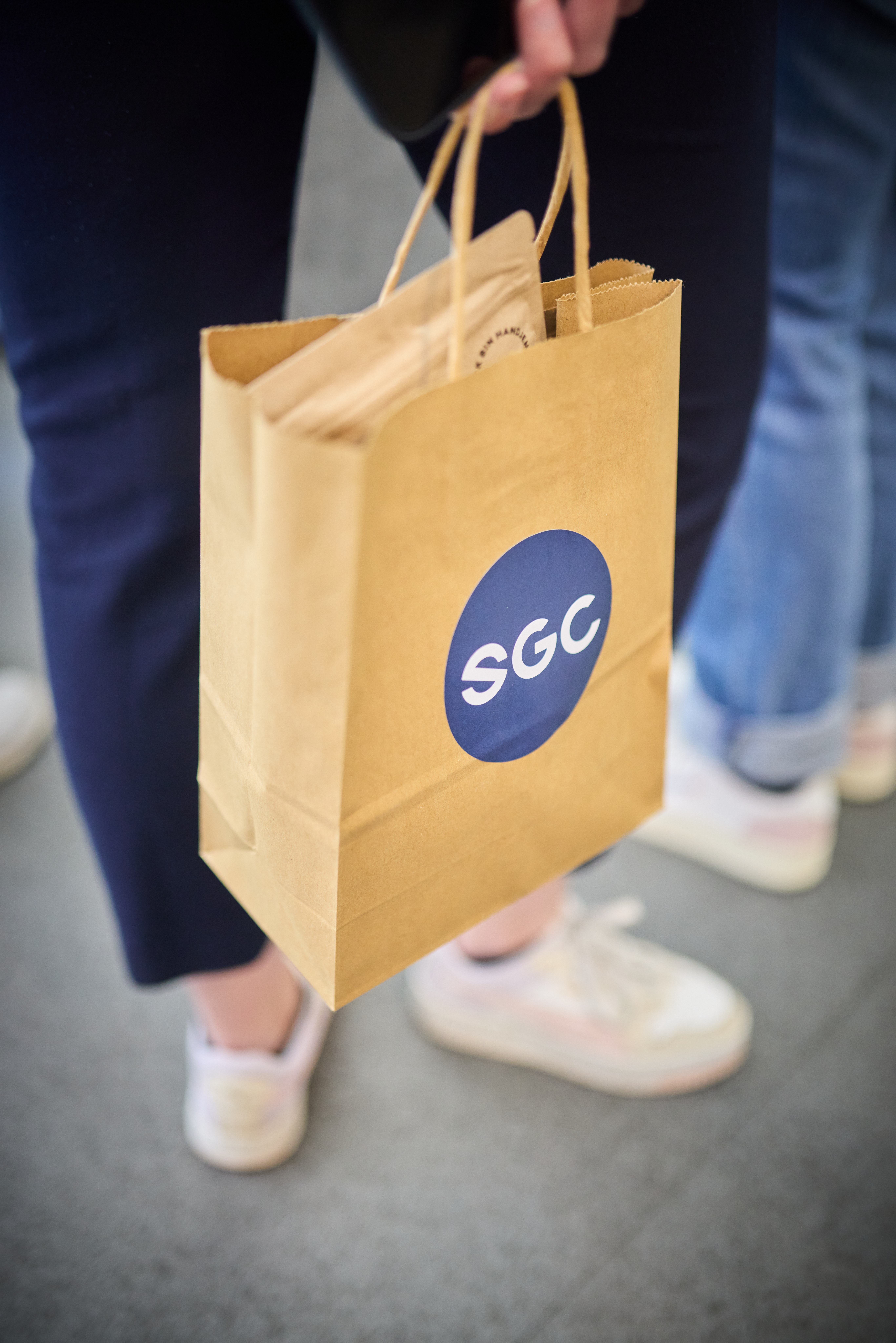 Person hält eine braune Papiertüte mit blauem SGC-Logo und Papierinhalt in der Hand.