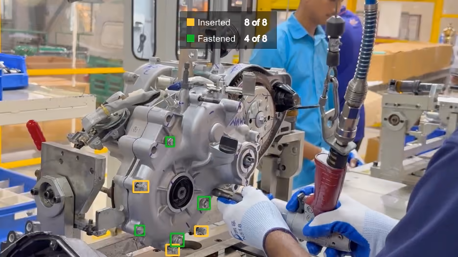 A factory worker assembling an engine casing, with a computer vision system detecting and overlaying status tracking for inserted and fastened bolts.