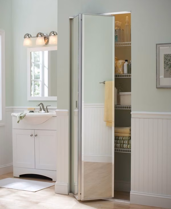 Mirrored bifold closet door folded open beside a bathroom vanity, revealing shelved towels and linens