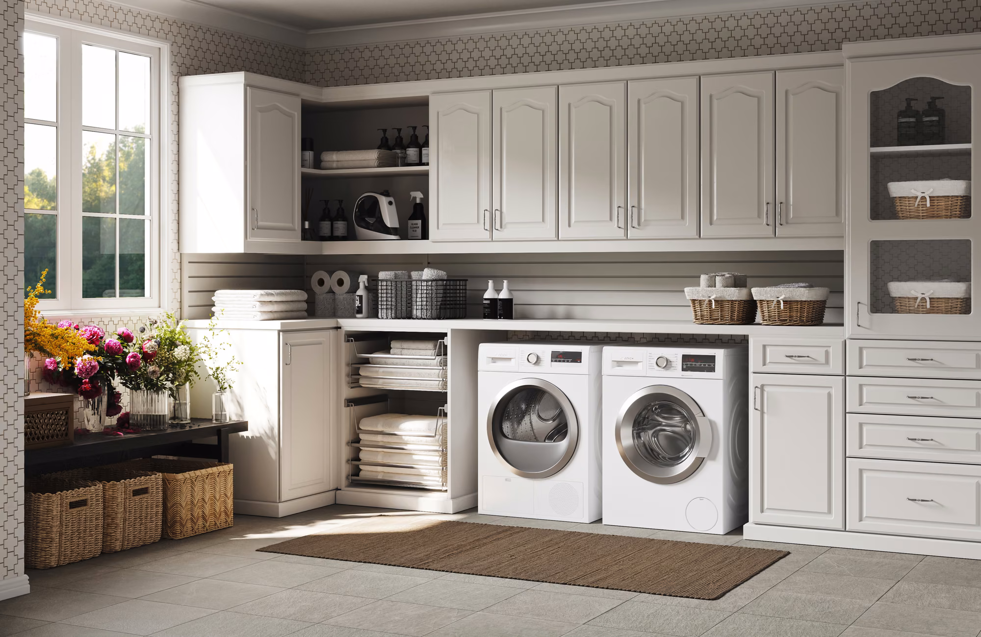 Traditional white laundry room with arched raised-panel cabinet doors, a glass-front upper cabinet holding baskets, pull-out linen shelves, and side-by-side front-load machines under a continuous countertop.
