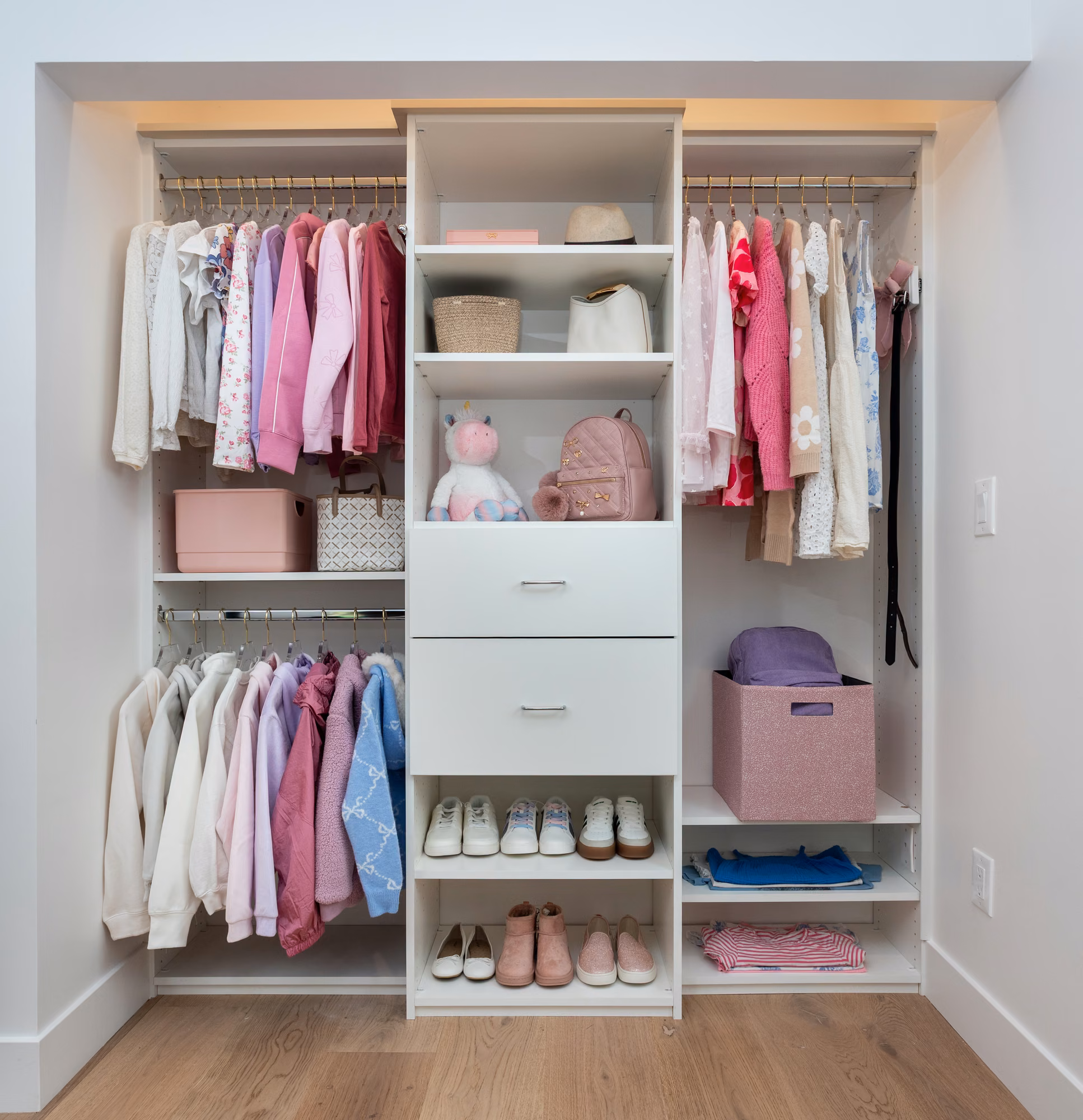Narrow white reach-in closet with two stacked hanging rods on the left, a single rod on the right, a center tower of shelves and drawers, shoe shelves, and fabric bins.