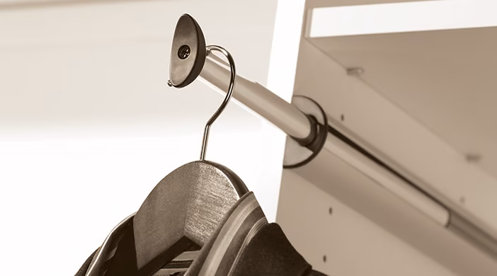 A matte chrome valet rod extended from a white closet panel with a single dark garment on a hanger.