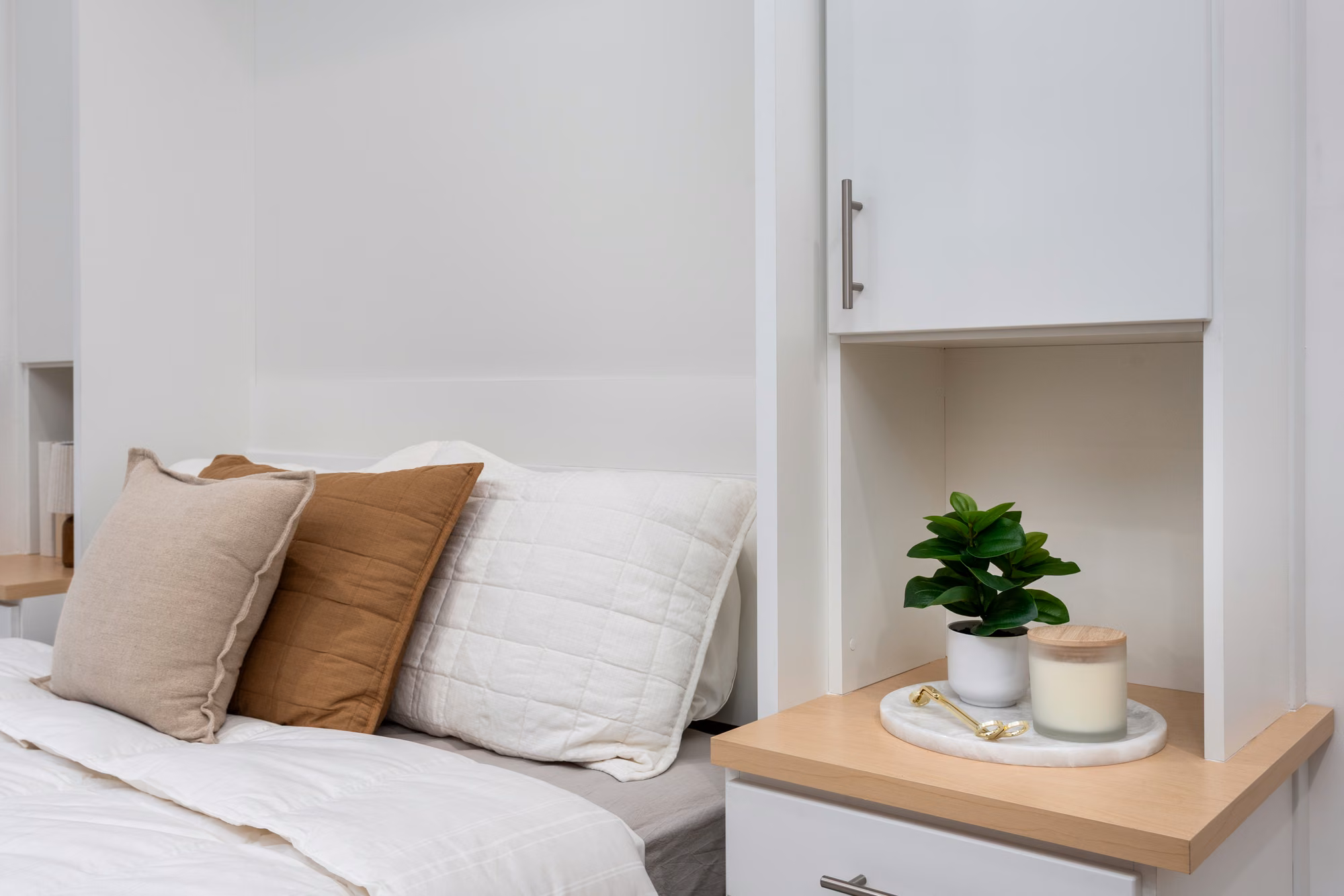 Close-up of a made Murphy bed beside a built-in shelf holding a small plant.