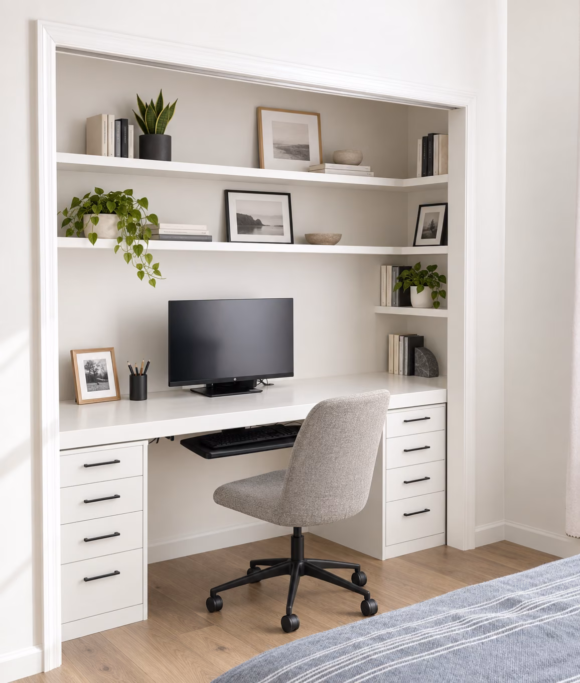 Closet converted into a built-in home office with open shelving, a desk, keyboard tray, and drawers, beside a bed.