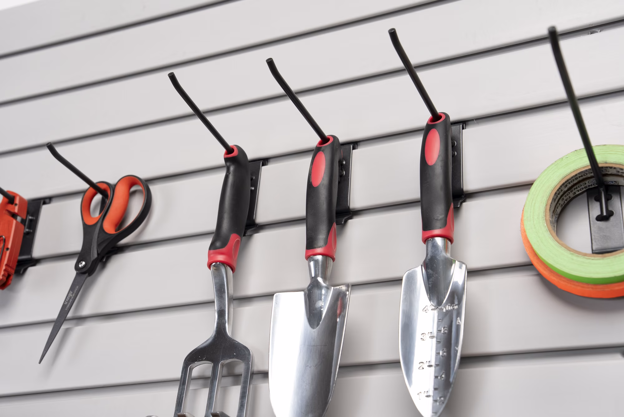 Close-up of garden trowels, shears, and tape hung on slatwall hooks.