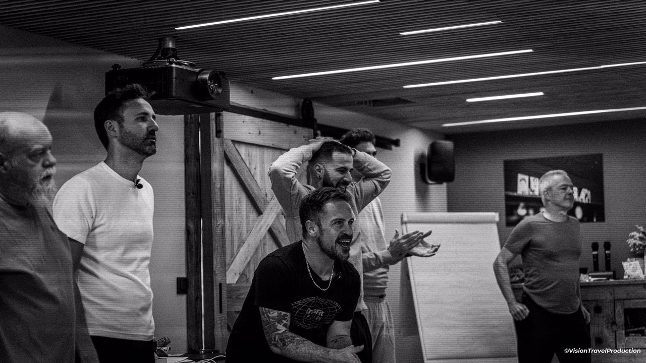 Six hommes dans une pièce, dont Morgan Cordelet, certains sont debout et font des gestes, pour soutenir d'autres personnes qui pratiquent des exercices. 