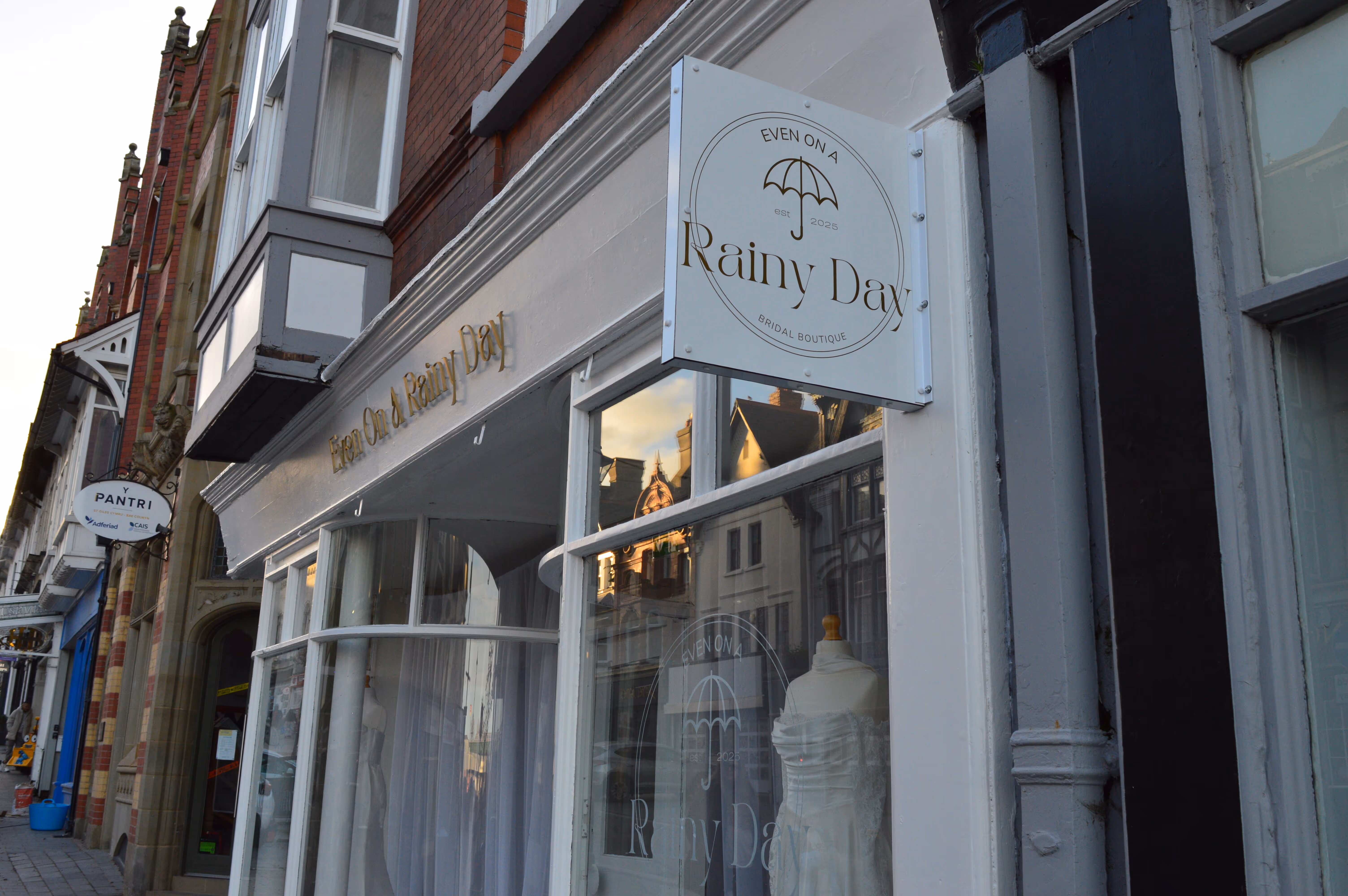 Exterior of a bridal boutique named 'Even On a Rainy Day' with a mannequin wearing a wedding dress in the window.