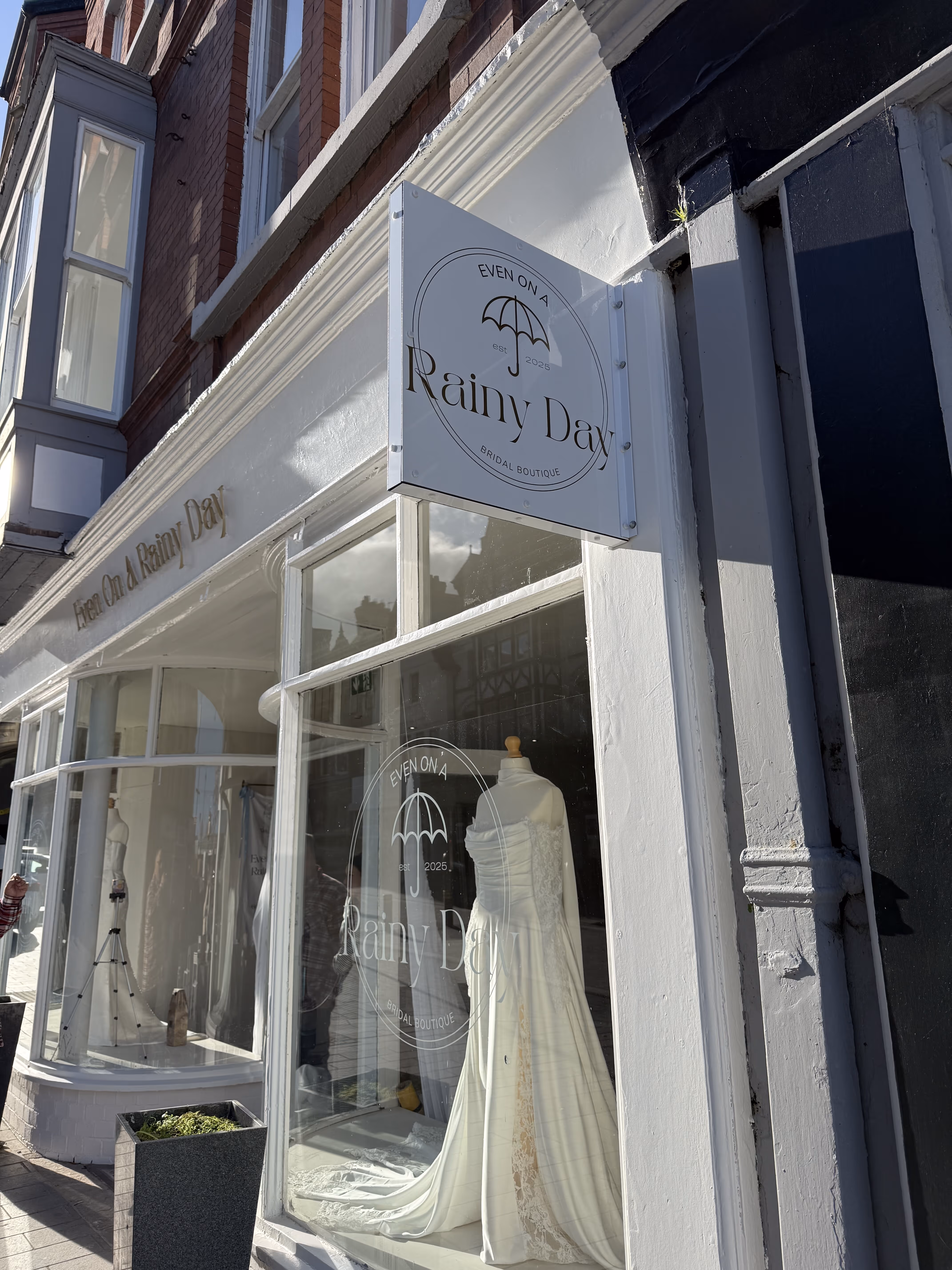 Front window of Even On A Rainy Day bridal boutique displaying a white wedding dress on a mannequin.