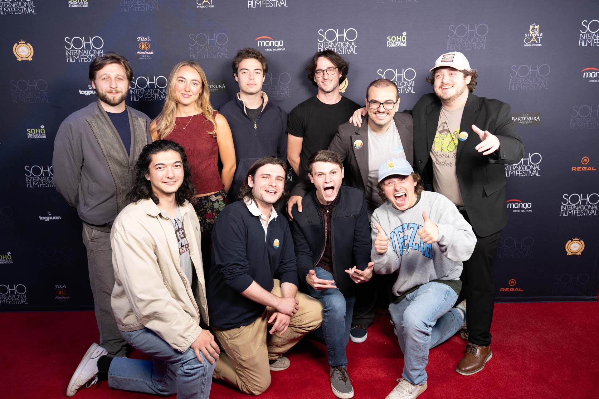Group of nine young adults posing and smiling on a red carpet at the Soho International Film Festival backdrop.
