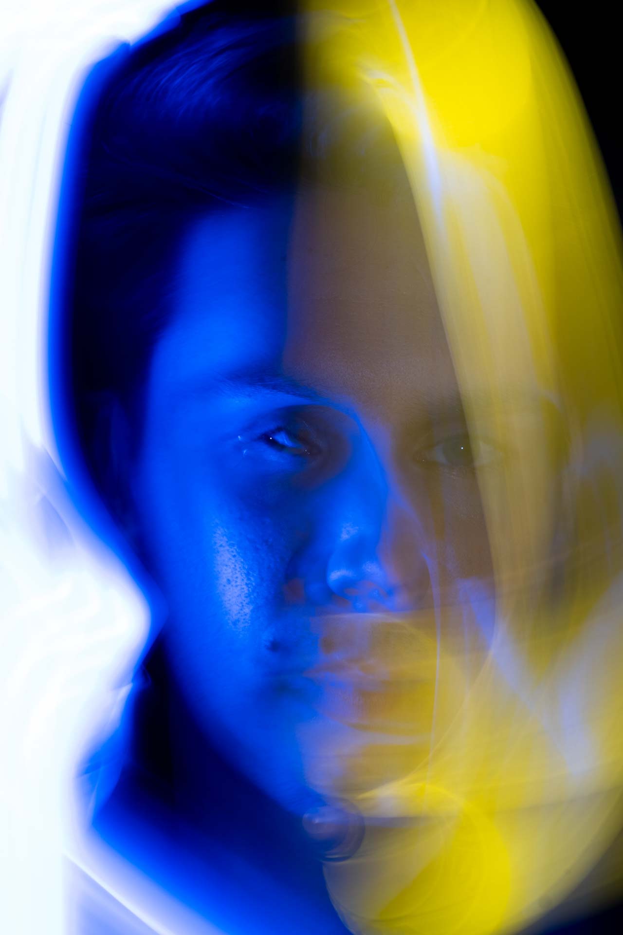 Blurred artistic portrait of a face with blue and yellow light streaks creating a symmetrical double exposure effect.