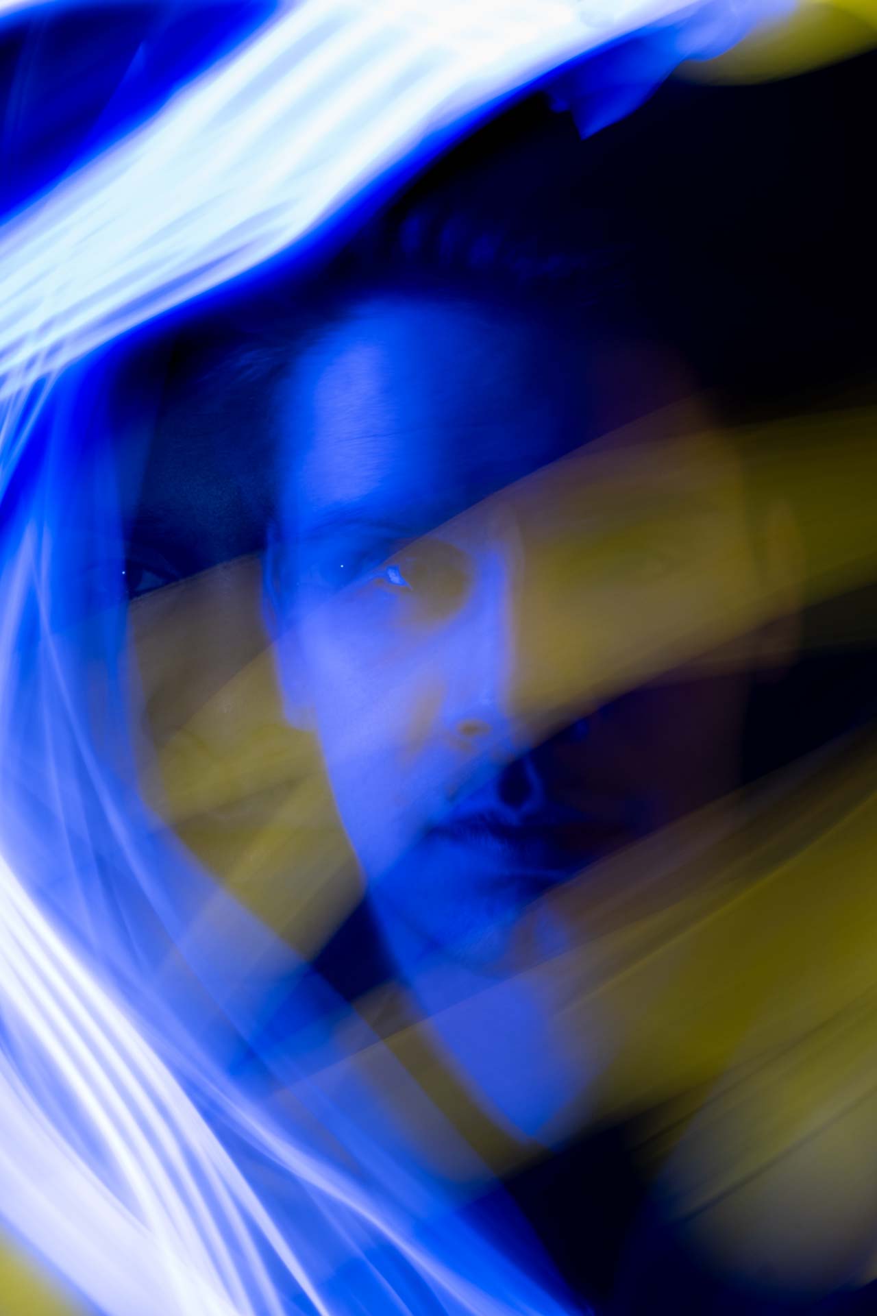 Blurred portrait of a person illuminated with blue and yellow light streaks creating an abstract, dynamic effect.