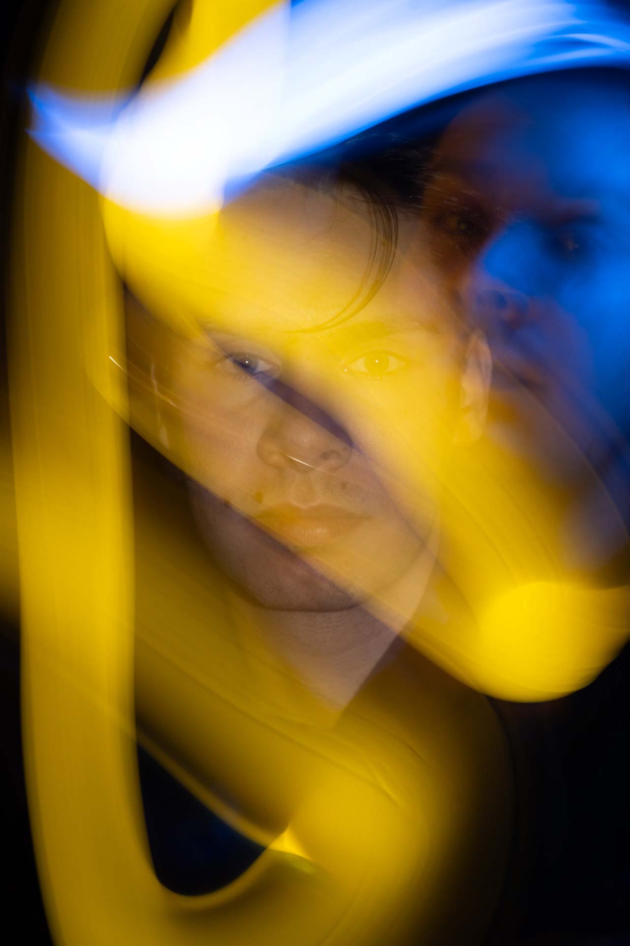 Blurred portrait of a man with yellow and blue light streaks creating an abstract effect.